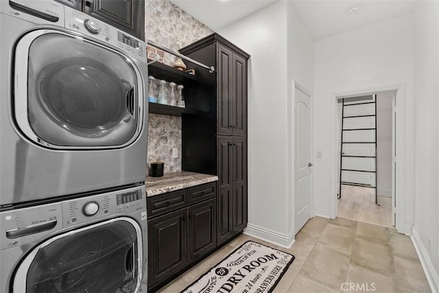 laundry room featuring cabinet space, baseboards, and stacked washer and dryer