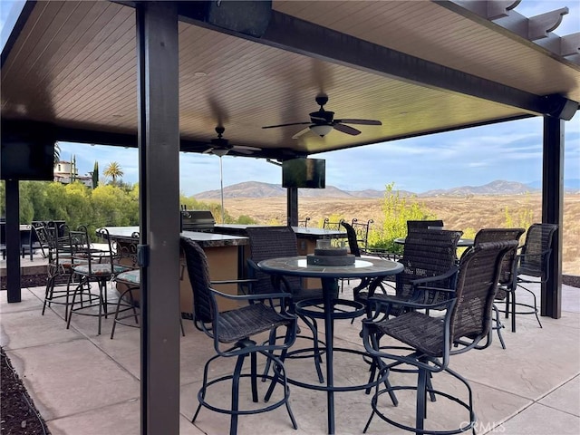 view of patio featuring ceiling fan, outdoor wet bar, a mountain view, and an outdoor kitchen