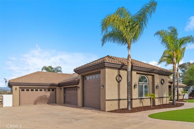 view of front of house with concrete driveway, a tiled roof, an attached garage, and stucco siding