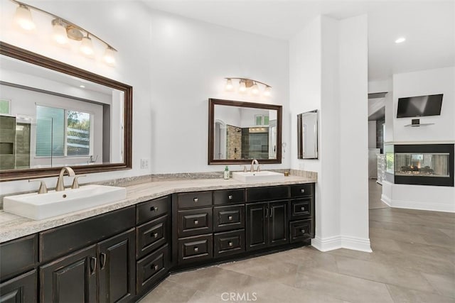 full bathroom featuring a sink, baseboards, a multi sided fireplace, and double vanity