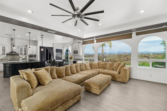 living area with baseboards, light wood-type flooring, ornamental molding, recessed lighting, and a ceiling fan