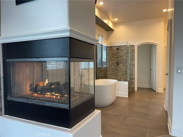 full bath featuring baseboards, a multi sided fireplace, a soaking tub, and a shower stall