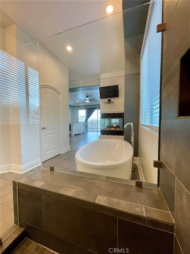 full bathroom with recessed lighting, baseboards, a multi sided fireplace, a soaking tub, and ceiling fan