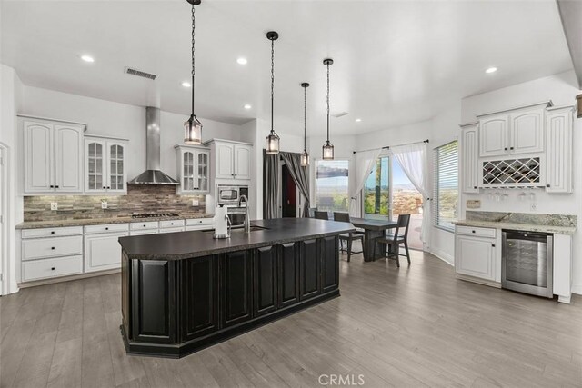 kitchen with beverage cooler, visible vents, stainless steel microwave, wall chimney range hood, and tasteful backsplash