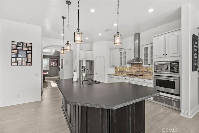 kitchen with a warming drawer, a sink, stainless steel appliances, arched walkways, and wall chimney range hood