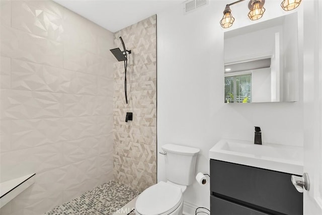 bathroom with visible vents, toilet, vanity, and a tile shower