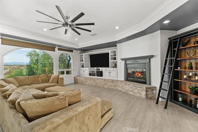 living area with ornamental molding, recessed lighting, wood finished floors, a glass covered fireplace, and a ceiling fan