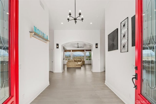 entrance foyer with visible vents, ceiling fan with notable chandelier, wood finished floors, arched walkways, and baseboards