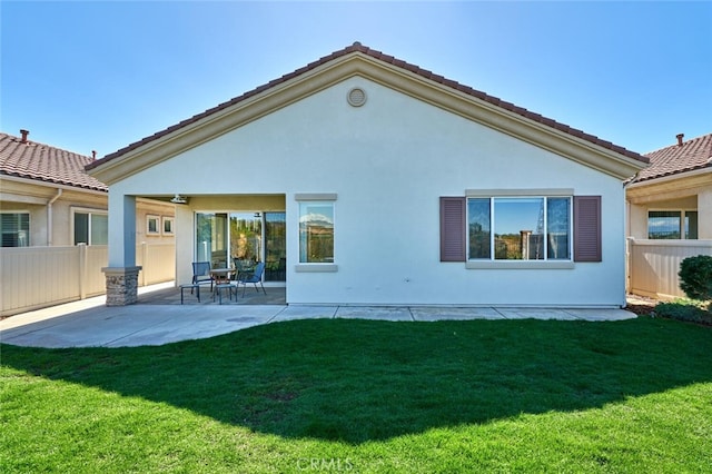 rear view of house with a yard, stucco siding, a patio area, fence, and a tiled roof