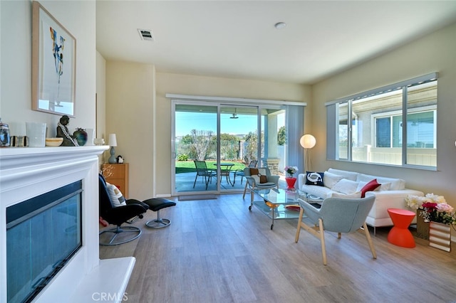 living area featuring visible vents, wood finished floors, and a glass covered fireplace