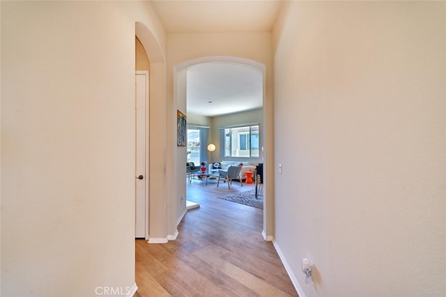 hallway featuring arched walkways, light wood-style flooring, and baseboards