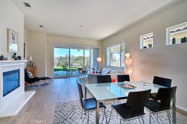 dining space featuring baseboards, visible vents, wood finished floors, and a glass covered fireplace