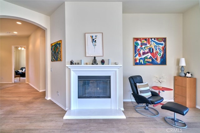 living area with arched walkways, a glass covered fireplace, baseboards, and wood finished floors