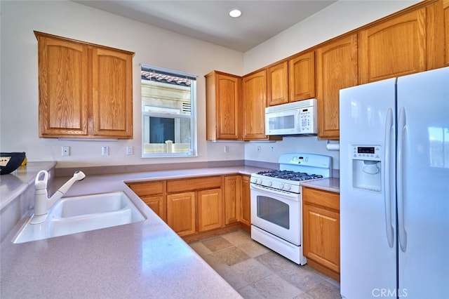 kitchen featuring brown cabinets, recessed lighting, light countertops, a sink, and white appliances