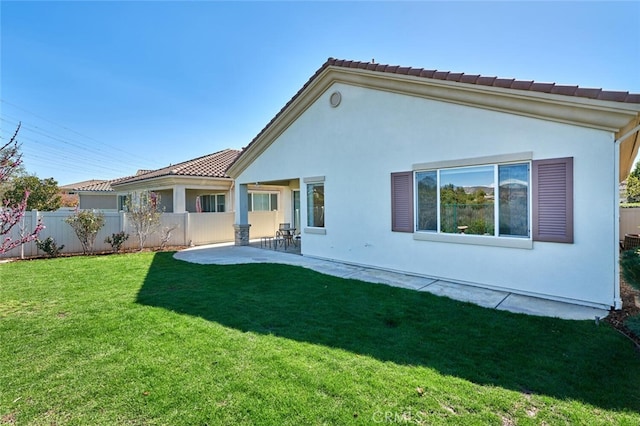 rear view of property featuring a lawn, a tile roof, fence, a patio area, and stucco siding