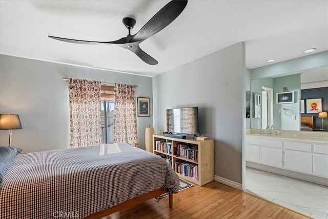 bedroom featuring baseboards, ceiling fan, light wood-style flooring, ensuite bath, and a sink