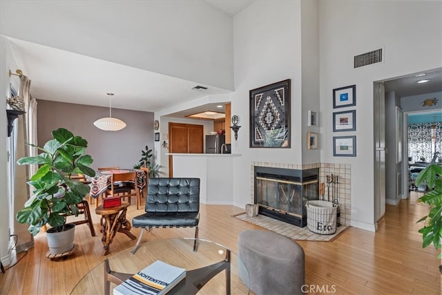 living area with a tiled fireplace, visible vents, and wood finished floors