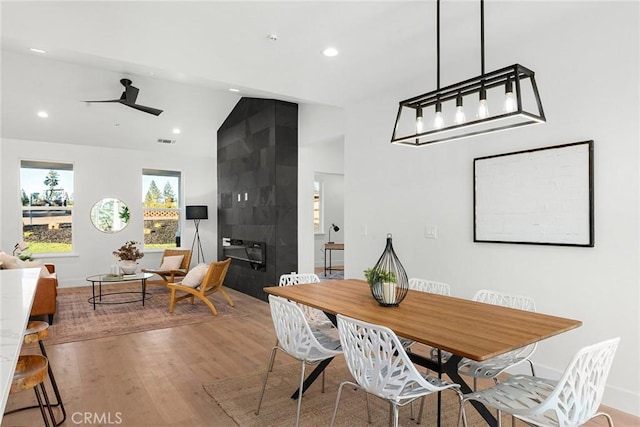 dining space with lofted ceiling, a tiled fireplace, wood finished floors, and recessed lighting