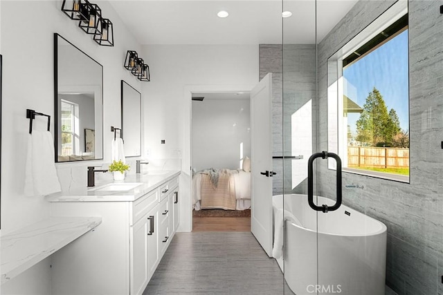 ensuite bathroom with a healthy amount of sunlight, a freestanding tub, connected bathroom, and a sink