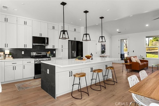 kitchen featuring visible vents, light wood-style floors, appliances with stainless steel finishes, backsplash, and a center island