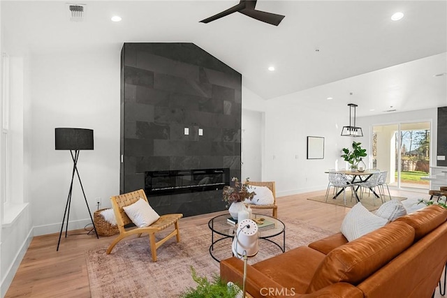 living room with light wood-type flooring, visible vents, vaulted ceiling, and a tiled fireplace