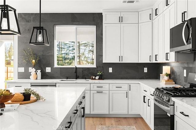 kitchen featuring stainless steel appliances, a sink, white cabinets, and light stone countertops