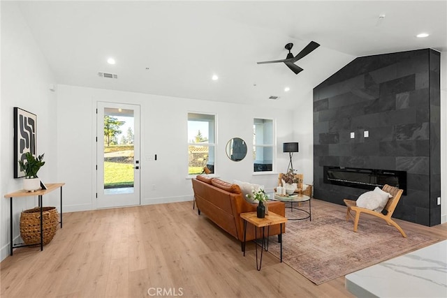 living room featuring a large fireplace, visible vents, baseboards, lofted ceiling, and light wood-style flooring