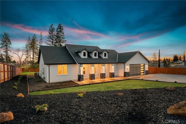 back of property at dusk with a garage, concrete driveway, fence, cooling unit, and stucco siding