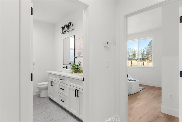 full bathroom featuring double vanity, baseboards, toilet, wood finished floors, and a sink