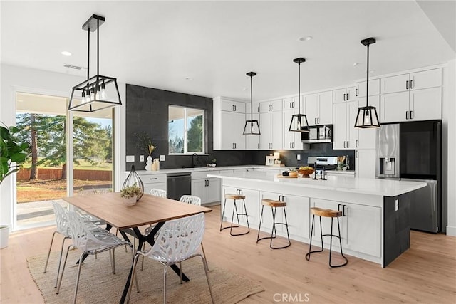 kitchen with light wood-style flooring, a kitchen island, appliances with stainless steel finishes, a breakfast bar, and backsplash