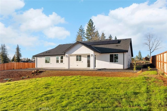 back of house with a yard, stucco siding, a fenced backyard, and roof mounted solar panels