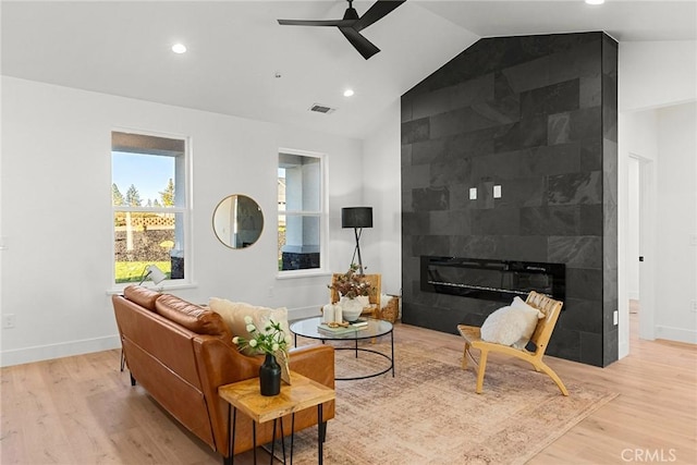 living area featuring visible vents, ceiling fan, vaulted ceiling, wood finished floors, and a tile fireplace