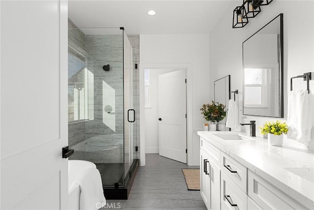 bathroom featuring double vanity, wood finished floors, a shower stall, a sink, and recessed lighting