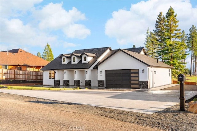 view of front facade featuring a garage, driveway, stone siding, fence, and stucco siding