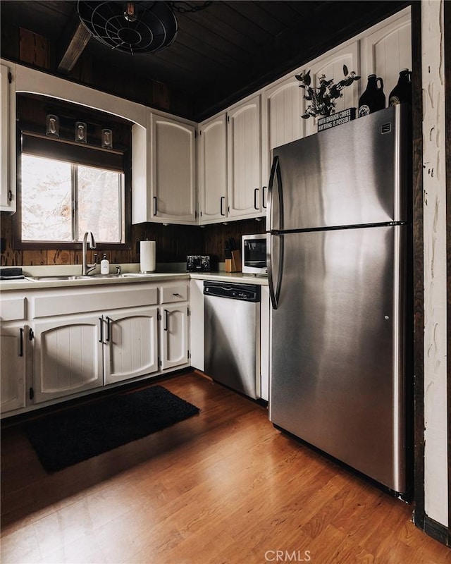 kitchen featuring stainless steel appliances, wood finished floors, a sink, and white cabinetry