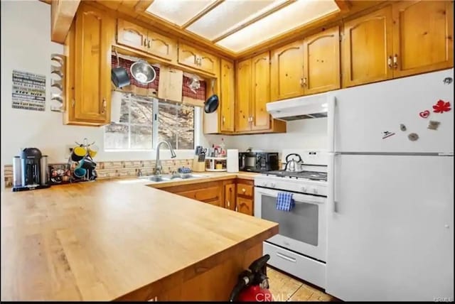 kitchen with brown cabinets, a sink, a peninsula, white appliances, and under cabinet range hood