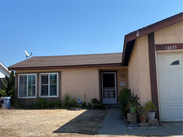 property entrance with a garage, roof with shingles, and stucco siding