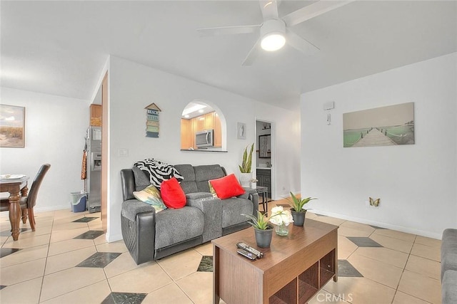 living room featuring light tile patterned floors, ceiling fan, arched walkways, and baseboards