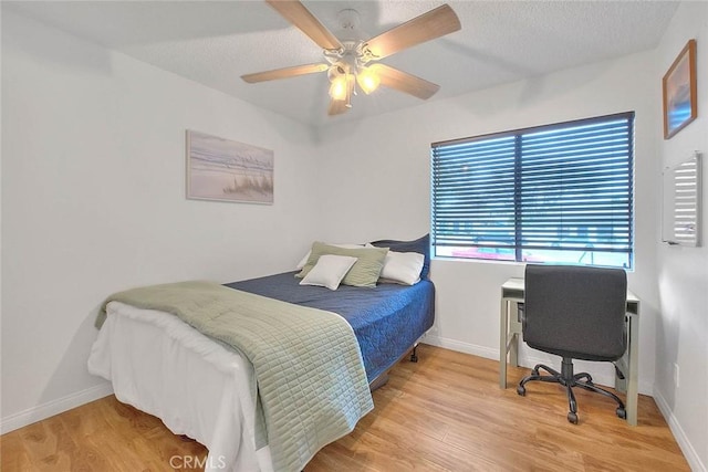 bedroom featuring ceiling fan, a textured ceiling, baseboards, and wood finished floors