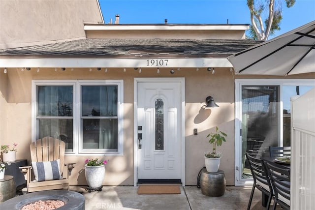 property entrance featuring a patio area, roof with shingles, and stucco siding