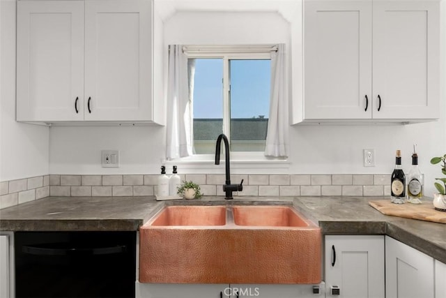 kitchen featuring white cabinetry, dark countertops, black dishwasher, and a sink