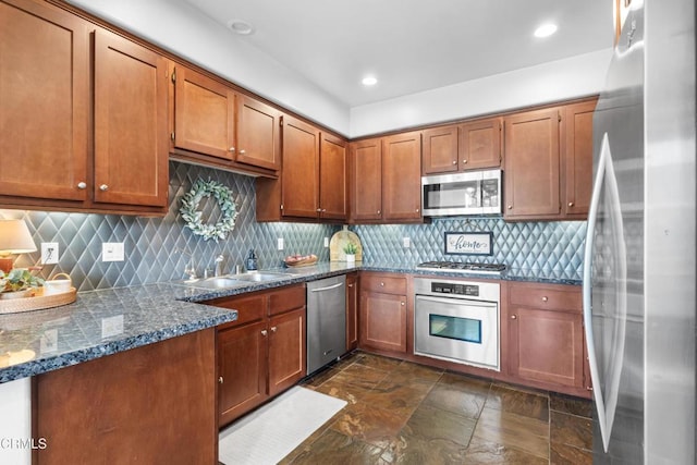 kitchen with brown cabinets, tasteful backsplash, appliances with stainless steel finishes, a sink, and dark stone counters