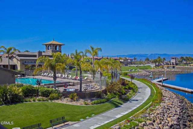 view of home's community featuring fence, a boat dock, a lawn, a water and mountain view, and a swimming pool