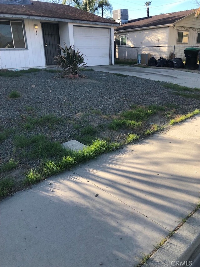 exterior space featuring a garage, driveway, fence, and central AC