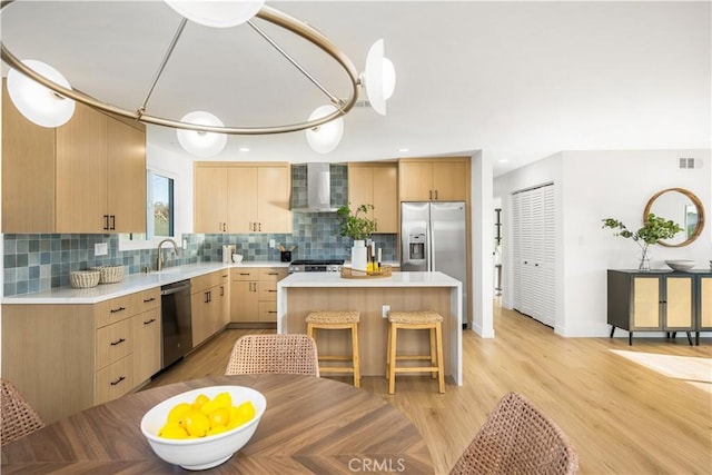 kitchen featuring light brown cabinetry, a sink, appliances with stainless steel finishes, wall chimney range hood, and light countertops