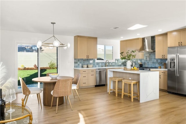 kitchen with a center island, light countertops, a kitchen breakfast bar, stainless steel appliances, and wall chimney exhaust hood