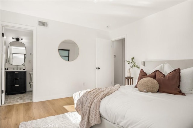 bedroom featuring visible vents, ensuite bathroom, baseboards, and wood finished floors