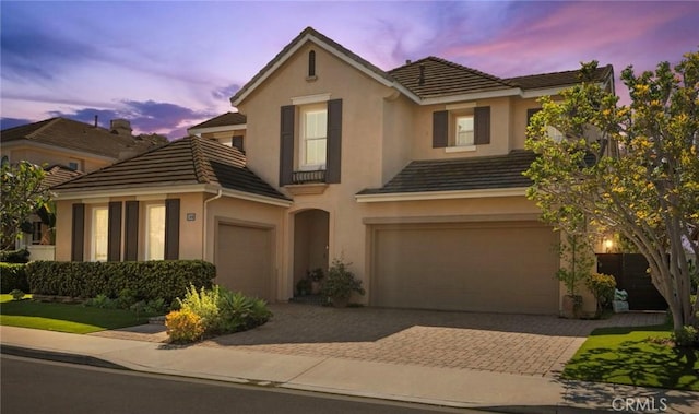 traditional-style home with a tiled roof, decorative driveway, a garage, and stucco siding