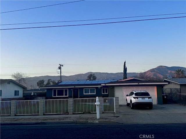 ranch-style house featuring a garage, solar panels, concrete driveway, a fenced front yard, and a mountain view