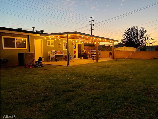 back of house at dusk with a yard, a patio area, fence, and stucco siding